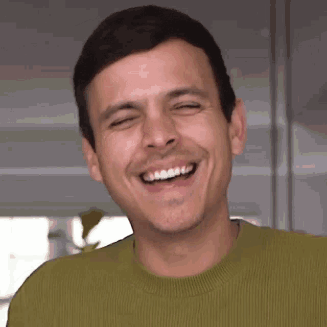 a man in a green sweater is laughing with his eyes closed