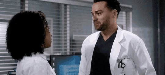 a man in a lab coat is talking to a woman in a scrub top .