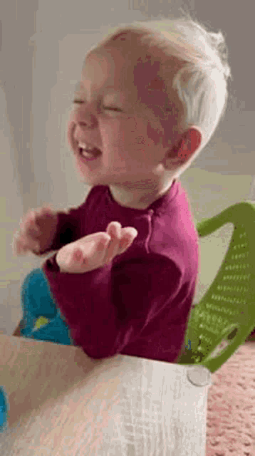 a baby is sitting at a table laughing with his hands outstretched .