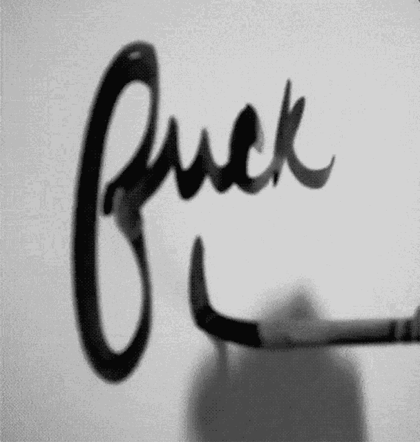 a black and white photo of a person writing the word fuck on a wall .