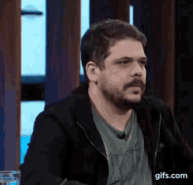 a man with a beard is sitting in front of a glass of water .