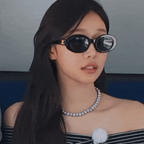 a woman wearing sunglasses and a pearl necklace is sitting on a boat .