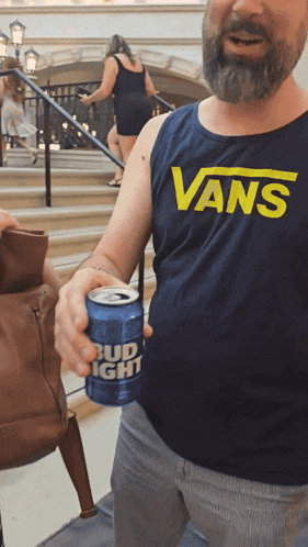 a man wearing a vans shirt is holding a bud light can