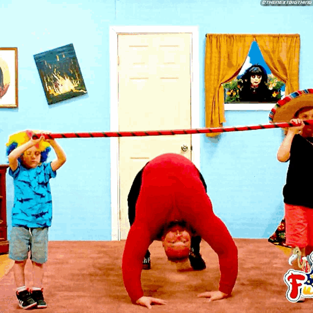 a man in a red jumpsuit is doing a handstand while a boy in a sombrero watches