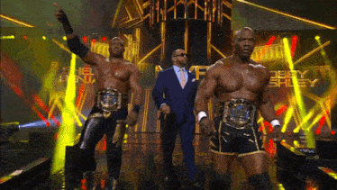 a man in a suit stands between two wrestlers wearing belts that say debby shley on them