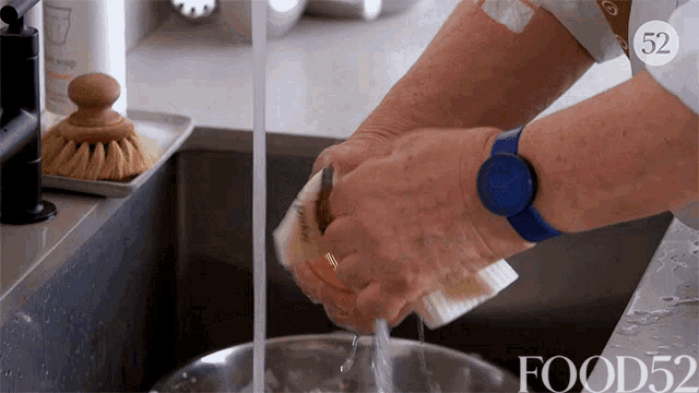 a person wearing a blue watch is washing dishes in a kitchen sink with food52 written on the bottom