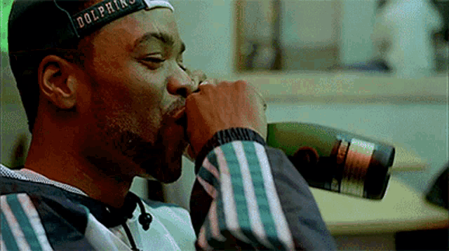 a man wearing a dolphins hat is drinking a bottle of beer