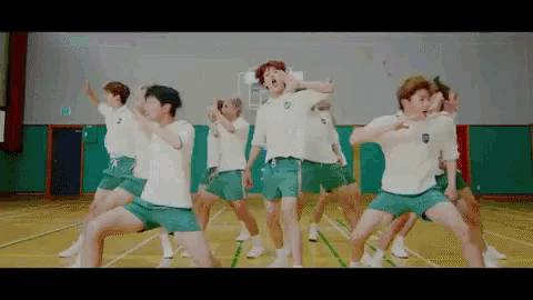 a group of young men in green shorts are dancing on a basketball court .
