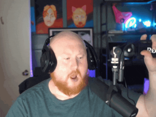 a bald man with a beard wearing headphones stands in front of a microphone holding a box that says du