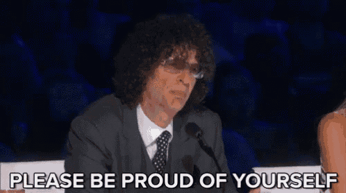 a man in a suit and tie is sitting in front of a microphone and saying please be proud of yourself
