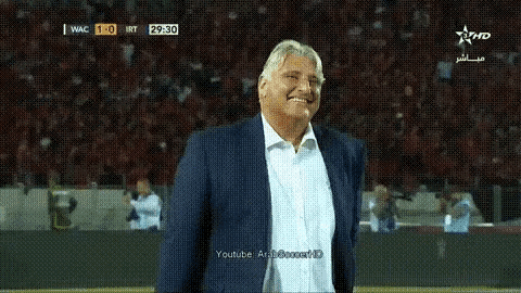 a man in a suit and white shirt is smiling in front of a crowd while watching a soccer game on youtube