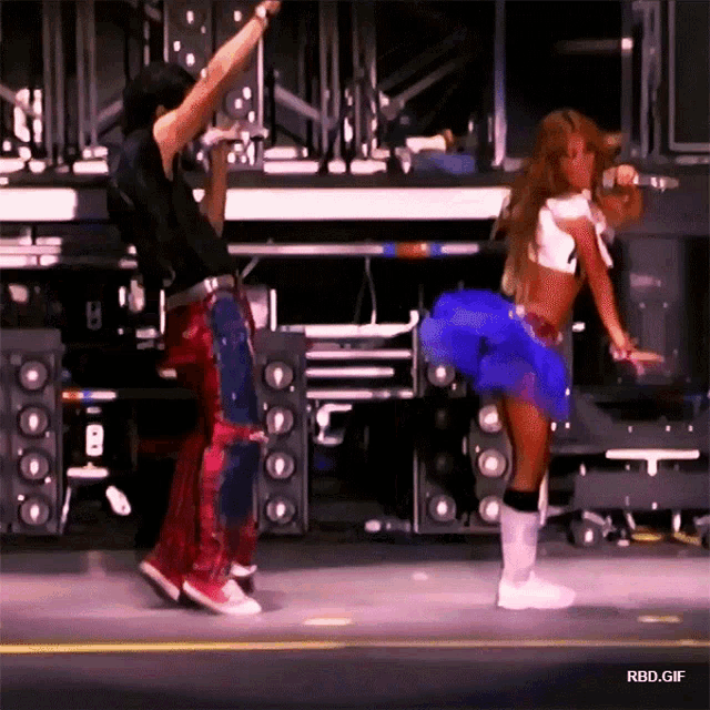 a woman in a blue skirt is dancing on stage with a man in a black shirt