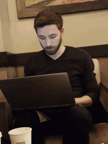 a dunkin donuts cup sits next to a man working on his laptop