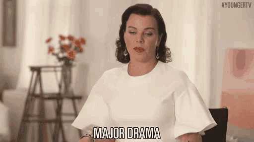 a woman in a white dress is sitting at a table with her eyes closed and says major drama .
