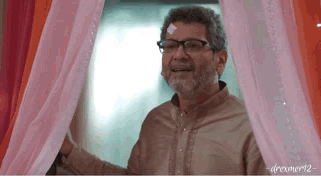 a man with glasses is standing in front of a pink curtain