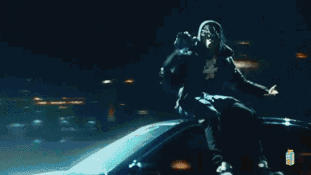 a man is sitting on the roof of a car at night holding a microphone .