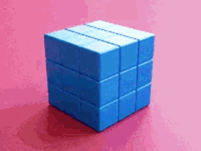 a blue cube is sitting on top of a pink surface .
