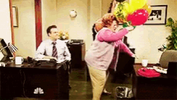 a woman is holding a bunch of balloons while a man sits at a desk