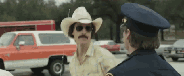 a man in a cowboy hat is talking to a police officer in a parking lot