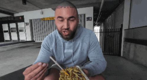 a man is eating noodles with a fork in front of a building with the number 50 on it