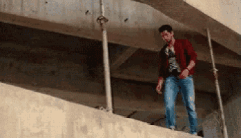 a man in a red jacket and blue jeans is standing on a balcony .