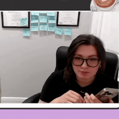 a woman wearing glasses is sitting in a chair and looking at her phone