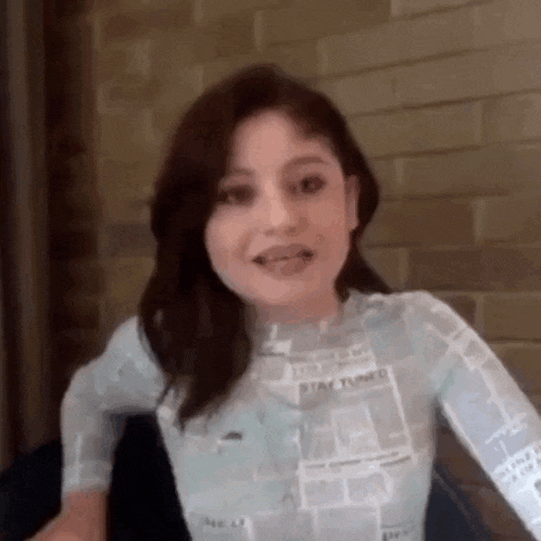 a woman is sitting in front of a brick wall and making a funny face with her tongue out .