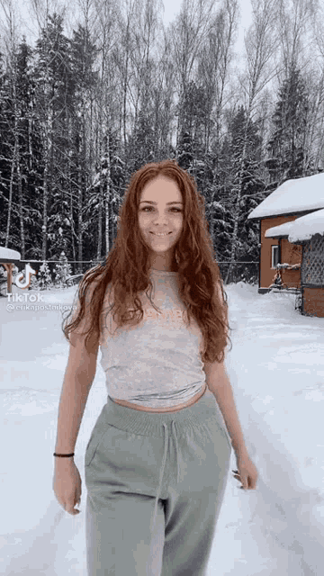 a woman with red hair is standing in the snow wearing green sweatpants and a crop top .