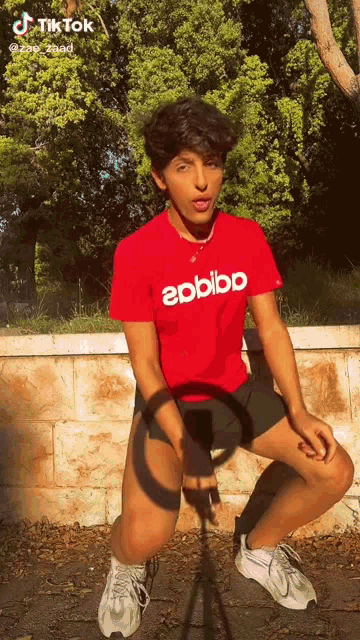 a young man wearing a red eobibb t-shirt is kneeling down