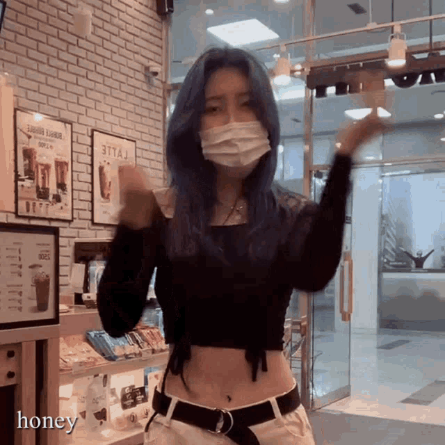 a woman with blue hair wearing a face mask stands in front of a glass door
