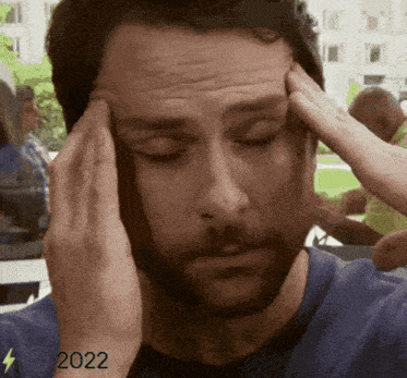 a man with a beard is holding his head with his hands .