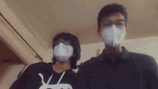 two people wearing face masks are standing next to each other in a room .