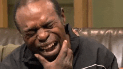 a man is sitting on a couch laughing with his eyes closed and his hand on his chin .