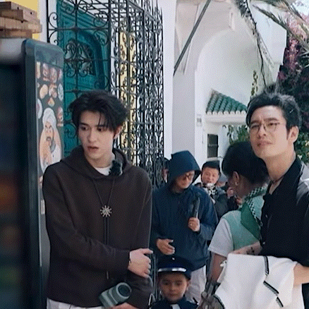 a group of people are standing outside of a building . one of the men is holding a camera .