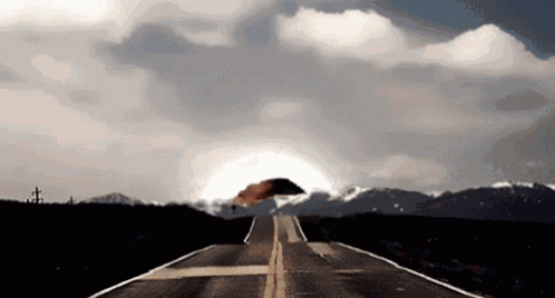 a person holding an umbrella is walking down a road with mountains in the background