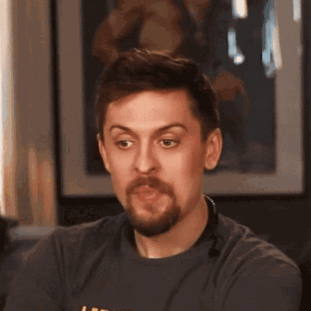 a man with a beard is wearing a gray shirt that says ' l.a.t.c. ' on it
