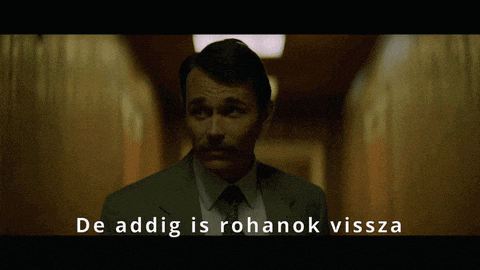 a man in a suit and tie is standing in a hallway with the words de addig is rohanok vissza behind him