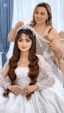 a woman is putting a tiara on the head of a woman in a wedding dress