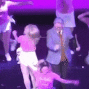 a group of people are dancing on a stage in front of a purple light .