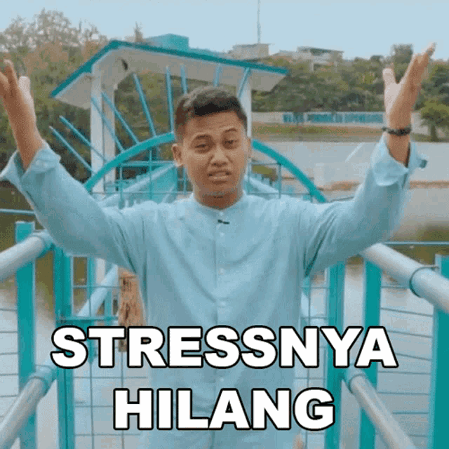 a man in a blue shirt is standing on a bridge with his arms outstretched and the words stressnya hilang written above him
