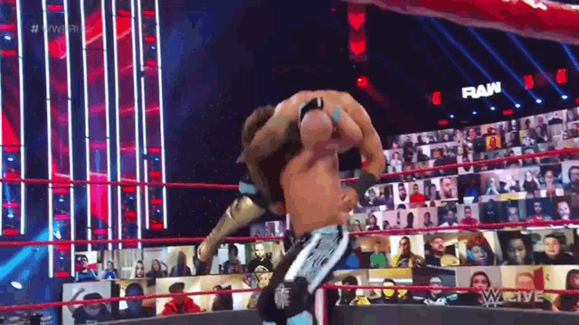 two men are wrestling in a wrestling ring while a crowd watches .