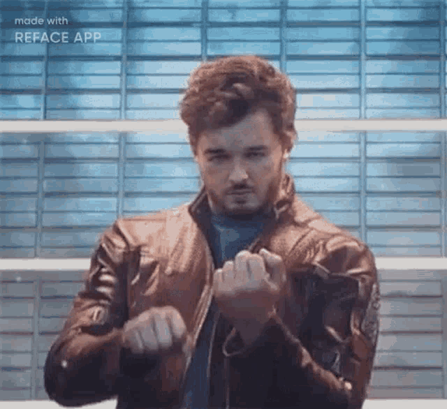 a man in a leather jacket is making a fist in front of a blue wall .