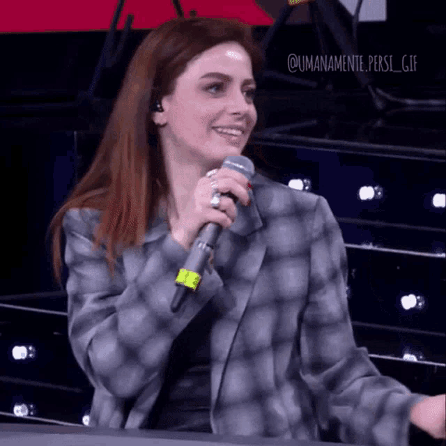 a woman in a plaid jacket is holding a microphone and smiling ..