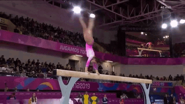 a female gymnast is doing a handstand on a balance beam in front of a crowd at a 2019 competition