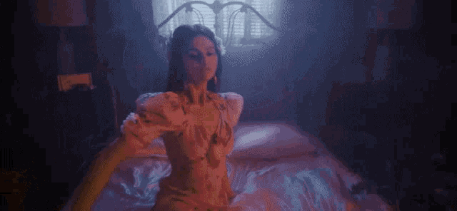 a woman in a pink dress is sitting on a bed in a dark room .
