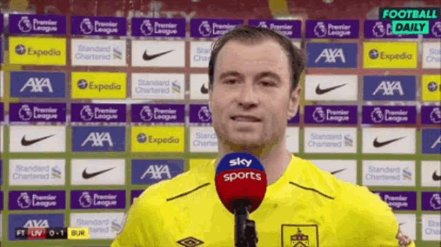 a man in a yellow shirt is talking into a microphone in front of a wall of advertisements for various companies including axa