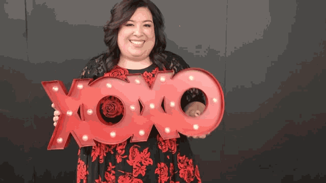 a woman in a red dress is holding a large red sign that says xoxo