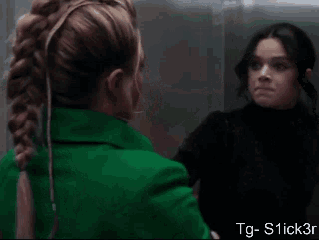 a woman in a green jacket is holding another woman 's hair in a ponytail
