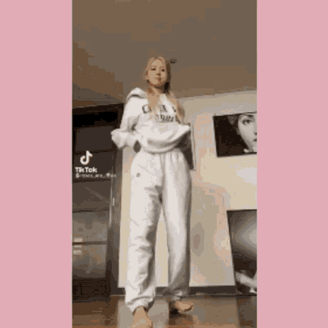 a woman is standing in a room wearing white sweatpants and a white hoodie .