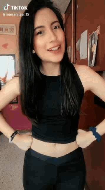 a woman wearing a black crop top and black pants is standing with her hands on her hips